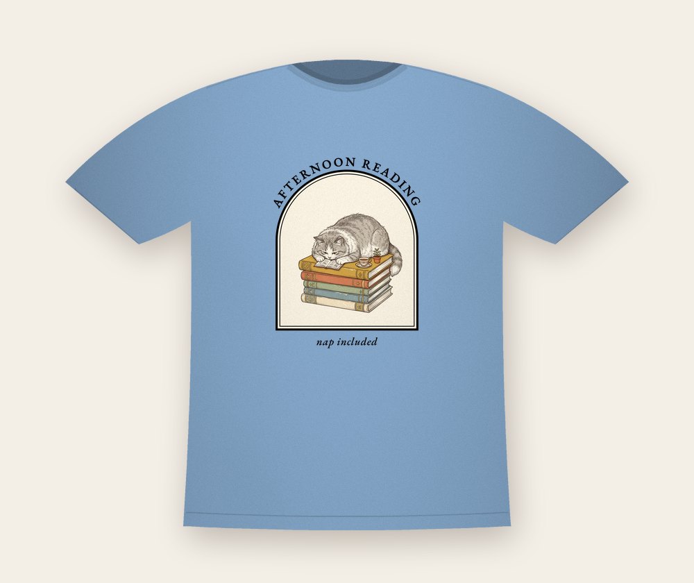 Light blue T-shirt with a fluffy cat asleep on a stack of colorful books, with the text Afternoon reading